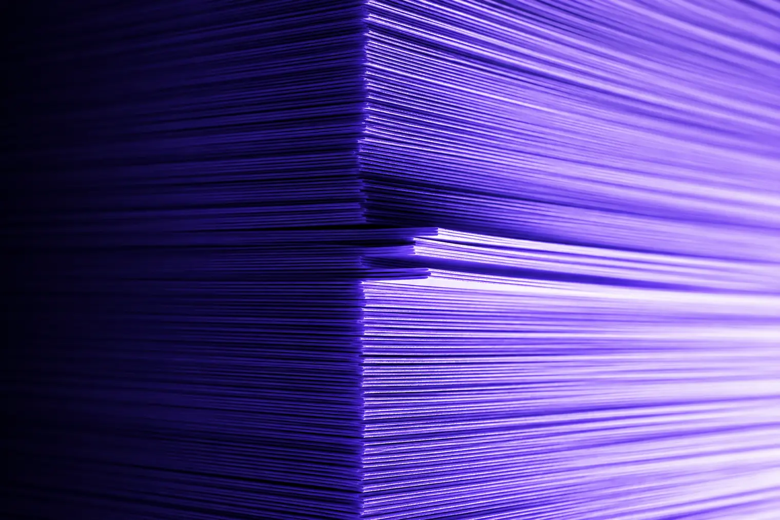 The cut edges of a deep stack of paper, lit from one side.